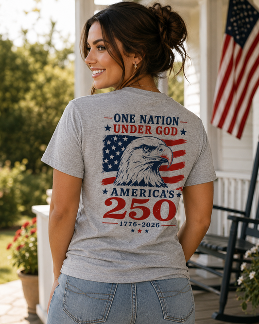 Woman wearing a t-shirt with 'One Nation Under God America's 250' design on a porch with an American flag in the background.